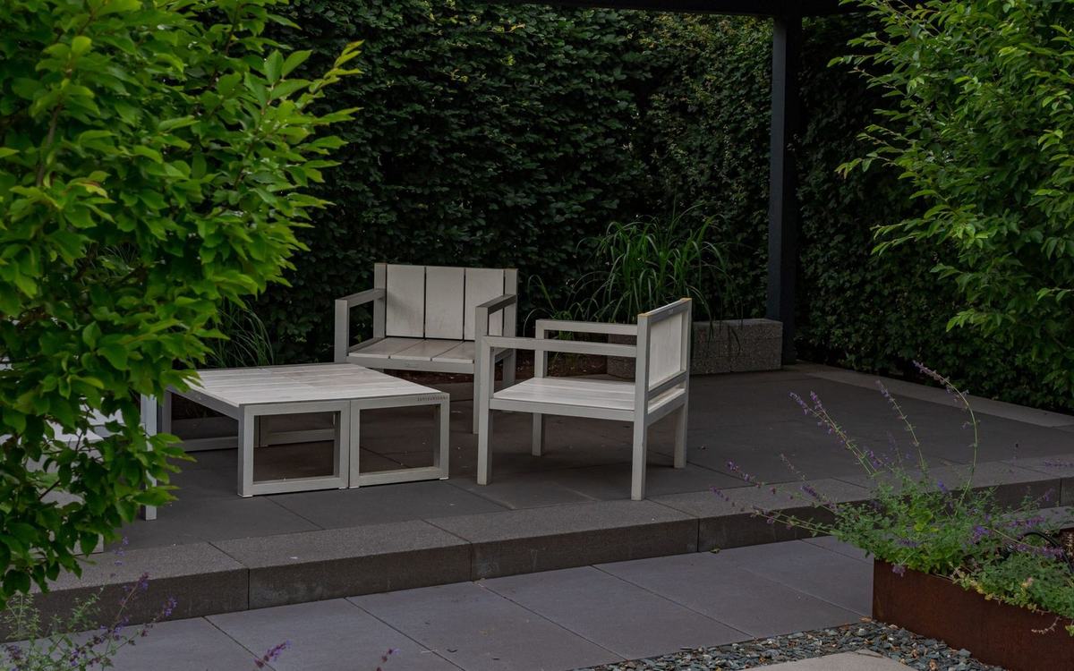 Modern paved garden terrace with outdoor furniture beside a clipped hedge