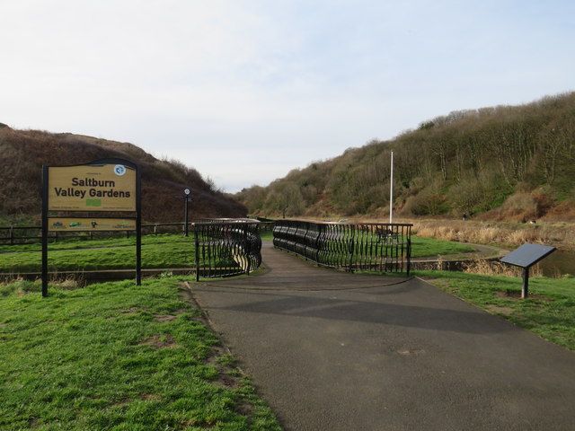 Entrance to Saltburn Valley Gardens with a path, footbridge and wooded valley side